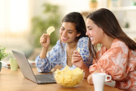 Dos mujeres en casa comiendo barcos de patatas viendo películas en el portátil