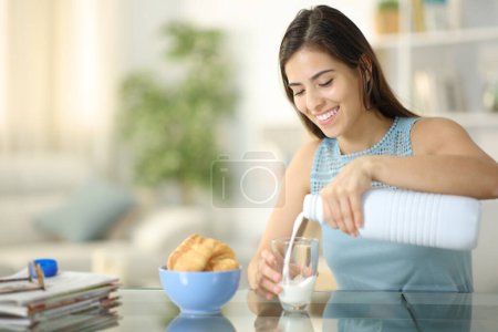 Téléchargez les photos : Femme qui boit du lait et de la boulangerie assis à la maison - en image libre de droit