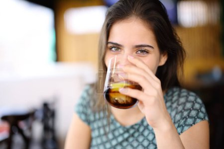Foto de Mujer feliz bebiendo refresco mirándote sentado en el interior de un bar - Imagen libre de derechos