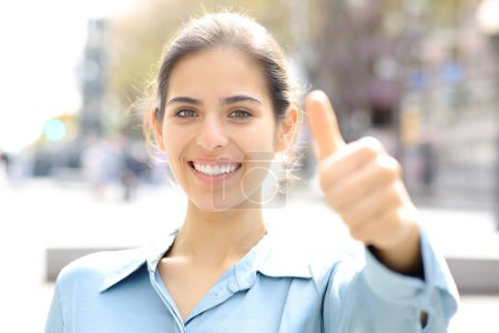 Téléchargez les photos : Femme heureuse geste pouces vers le haut à la caméra dans la rue - en image libre de droit