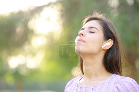 Téléchargez les photos : Femme respirant et méditant avec écouteur dans un parc - en image libre de droit