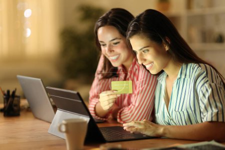 Foto de Dos teletrabajadores comprando en línea con tableta y tarjeta de crédito en casa en la noche - Imagen libre de derechos