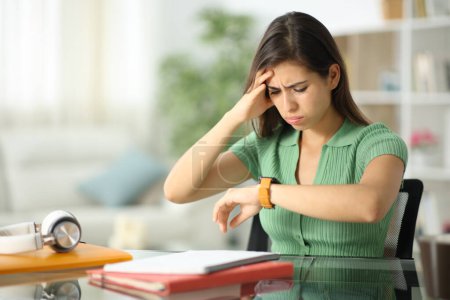Worried student is checking her smartwatch sitting at home