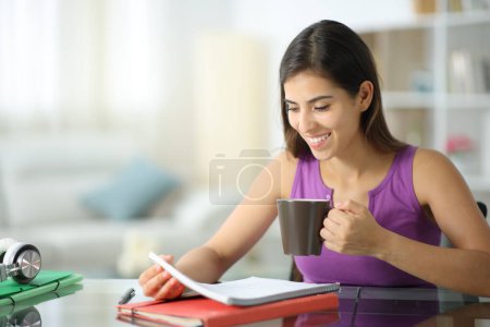 Foto de Estudiante feliz memorizando notas y tomando café en casa - Imagen libre de derechos