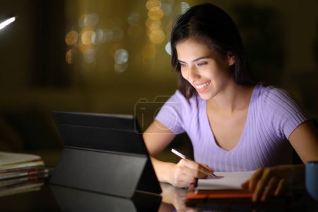 Photo for Happy student using tablet to e-learn late in the night at home - Royalty Free Image