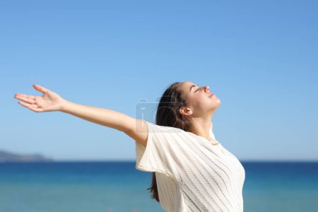 Téléchargez les photos : Femme étendant les bras et respirant de l'air frais sur la plage - en image libre de droit