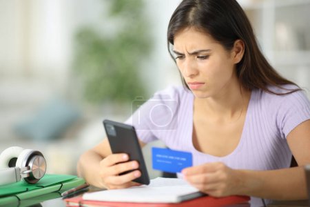 Photo for Worried student buying online with credit card and phone at home - Royalty Free Image