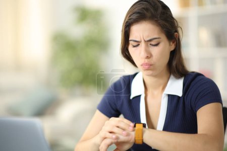 Foto de Mujer preocupada revisando smartwatch sentado en casa - Imagen libre de derechos