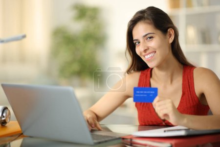 Glückliche Studentin schaut dich beim Online-Kauf mit Laptop und Kreditkarte an