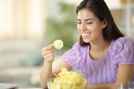 Foto de Mujer feliz comiendo papas fritas sonriendo sentada en casa - Imagen libre de derechos