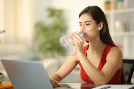 Téléchargez les photos : Étudiant eau potable de bouteille étudiant avec un ordinateur portable à la maison - en image libre de droit