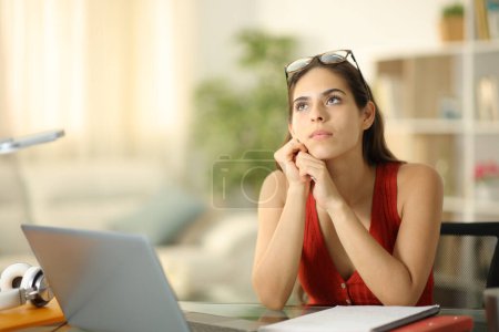 Serious student with a laptop thinking looking above at home