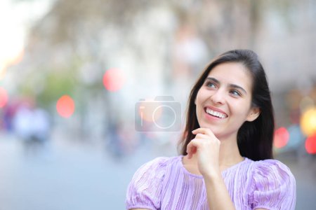 Téléchargez les photos : Vue de face portrait d'une femme heureuse pensant à côté dans la rue - en image libre de droit