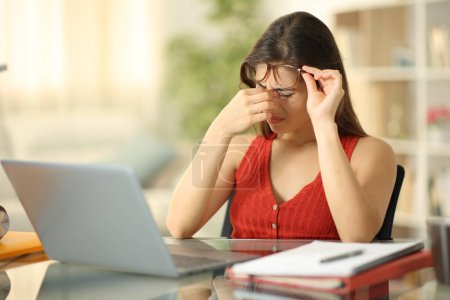 Téléchargez les photos : Étudiant portant des lunettes souffrant de fatigue oculaire avec un ordinateur portable à la maison - en image libre de droit