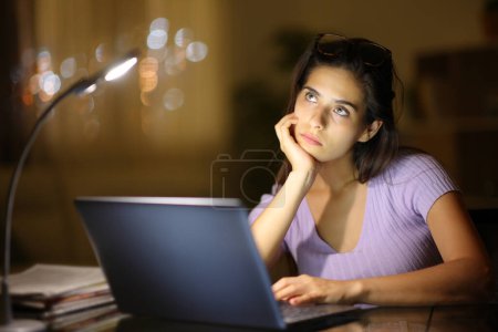 Foto de Pensativo mujer seria en casa con un ordenador portátil en la noche - Imagen libre de derechos