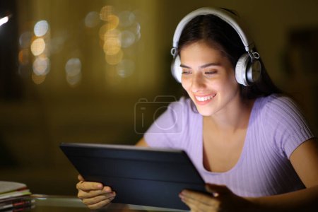 Glückliche Frau nutzt Tablet, um nachts zu Hause Videos anzuschauen