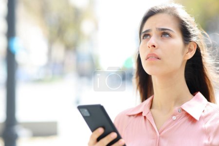 Besorgte Frau mit Handy schaut auf der Straße nach oben