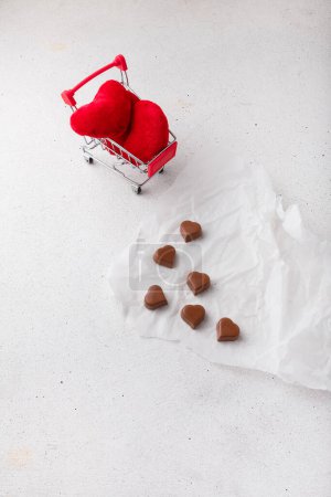 Téléchargez les photos : 14 février Chocolats en forme de coeur sur papier blanc, jouets coeur en tissu dans le chariot. Saint Valentin, cadeaux de lobbying, bonbons. Vente - en image libre de droit