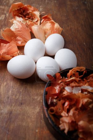 Weiße Eier und Zwiebelschalen auf dem rustikalen Tisch. DIY Ostereier Bio-Farbe aus natürlichen Pflanzen. Hausgemachte bunte festliche Ostereier. Kopierraum, vertikale Aufnahme
