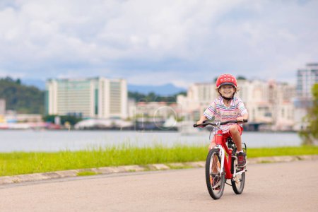 Téléchargez les photos : Enfant à vélo. Enfant à vélo dans un parc ensoleillé. Petit garçon profitant de balade à vélo sur son chemin vers l'école par une chaude journée d'été. Les enfants d'âge préscolaire apprennent à s'équilibrer à vélo dans un casque sûr. Sport pour enfants. - en image libre de droit