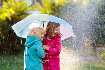 Photo for Kids with colorful umbrella playing in autumn shower rain. Little boy and girl in warm duffle coat play in a park by rainy weather. Fall outdoor fun for children. Kid catching rain drops. - Royalty Free Image