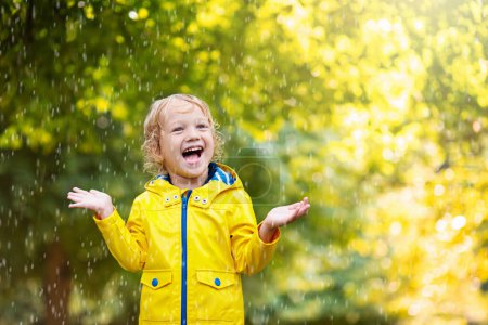 Foto de Los niños juegan bajo la lluvia de otoño. Niño jugando al aire libre en el día lluvioso. Un niño cogiendo gotas de lluvia bajo una fuerte ducha. Tormenta de otoño en un parque. Ropa impermeable para niño. Niños al aire libre por cualquier clima
. - Imagen libre de derechos