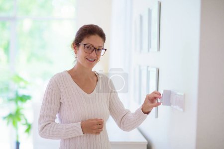 Mujer ajustando el termostato. Calefacción central. Cómoda temperatura del hogar. Regulador de climatización de ambiente femenino. Enfriamiento en el caluroso día de verano. Aire acondicionado interior. 