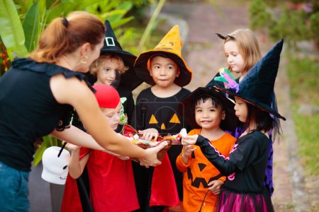 Photo for Kids trick or treat on Halloween night. Mixed race Asian and Caucasian children at decorated house door. Boy and girl in witch and vampire costume and hat with candy bucket and pumpkin lantern. - Royalty Free Image