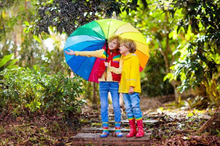 Téléchargez les photos : Enfant jouant sous la pluie d'automne. Enfant avec parapluie. Petit garçon courant dans un parc à l'automne. Amusement extérieur pour les enfants par tous les temps. Vêtements imperméables à l'eau, bottes et veste pour enfants. - en image libre de droit