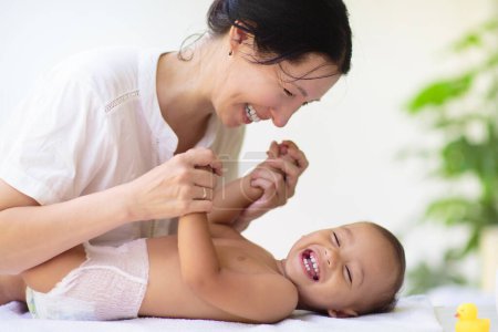 Photo for Mother changing diaper on newborn baby. Mom and laughing baby boy after bath or shower. Skin care for young kids. Asian woman changing nappy. Bathing and washing infant kid. - Royalty Free Image