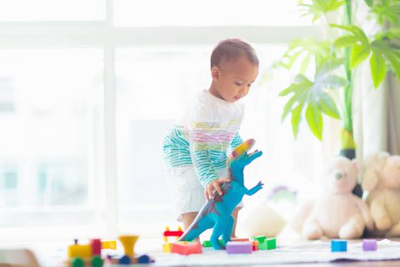 Photo for Adorable Asian baby boy learning to crawl and playing with colorful block toy in white sunny bedroom. Cute laughing child crawling on a play mat. Nursery, clothing and toys for little kids. - Royalty Free Image