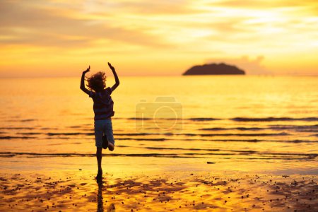 Photo for Child playing on ocean beach. Kid jumping in the waves at sunset. Sea vacation for family. Little boy running on exotic island during summer holiday. - Royalty Free Image