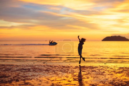 Foto de Niño jugando en la playa del océano. Un niño saltando en las olas al atardecer. Vacaciones en el mar para familia. Niño corriendo en la isla exótica durante las vacaciones de verano. - Imagen libre de derechos