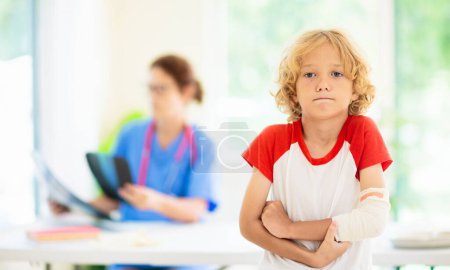 Photo for Child with arm injury at trauma and emergency care. Kid with elbow cast at health clinic. Doctor checking x-ray of injured little boy. Kids hospital. - Royalty Free Image