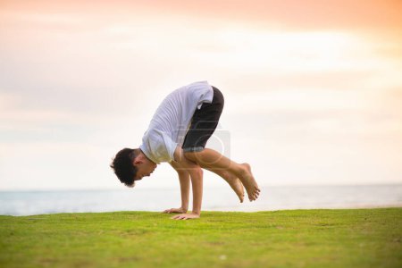 Photo for Teenager doing calisthenics exercise. Beach yoga at sunset. Teen boy exercising. Crow and peacock pose training. Sport for active young adult man. Arm balance asana. School child sports. - Royalty Free Image