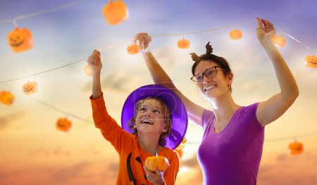 Photo for Family decorating home for Halloween celebration. Kids and mother hang pumpkin lantern lights trick or treat decoration. Kids decorate home. Children in witch costume and hat. Spooky Halloween fun. - Royalty Free Image