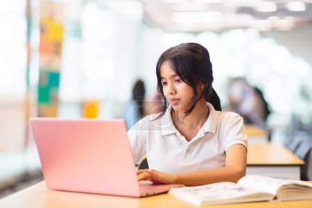 Photo for Asian girl with laptop in school. Student in classroom. Teenager in uniform doing homework with computer in library. Teen child studying for class. Kids study. Back to school. - Royalty Free Image