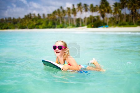 Photo for Child surfing on tropical beach. Family summer vacation in Asia. Kids swim in ocean water. Kid on surf body board. Little girl swimming in exotic sea. Travel with children. Water and beach sport. - Royalty Free Image