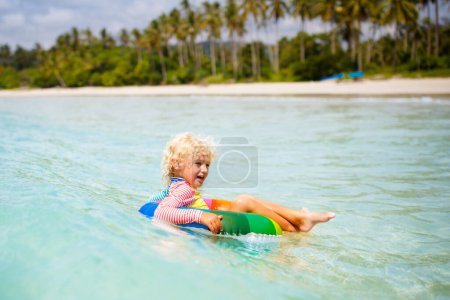 Foto de Niño con anillo inflable en hermosa playa. Un niño nadando en un mar exótico. Vacaciones en el océano con niño. Los niños juegan en la playa de verano. Agua divertida. Los niños nadan. Vacaciones familiares en isla tropical. - Imagen libre de derechos