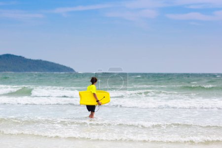 Photo for Teenage boy surfing on tropical beach. Family summer vacation in Asia. Kids swim in ocean water. Teenager on surf body board. Young adult swimming in exotic sea. Active water and beach sport. - Royalty Free Image