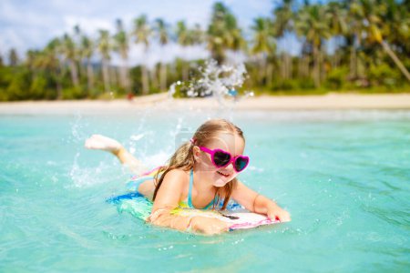 Téléchargez les photos : Surf pour enfants sur la plage tropicale. Vacances d'été en famille en Asie. Les enfants nagent dans l'eau de mer. Enfant sur planche de surf. Petite fille nageant dans la mer exotique. Voyagez avec des enfants. Sports nautiques et de plage. - en image libre de droit