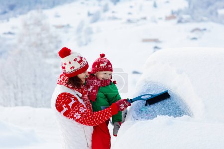 Téléchargez les photos : Mère et enfant brossant et pelletant la neige hors de la voiture après la tempête. Parent et enfant avec brosse d'hiver et racleur déblayage voiture familiale après blizzard de neige la nuit. Vacances de Noël dans les montagnes. - en image libre de droit