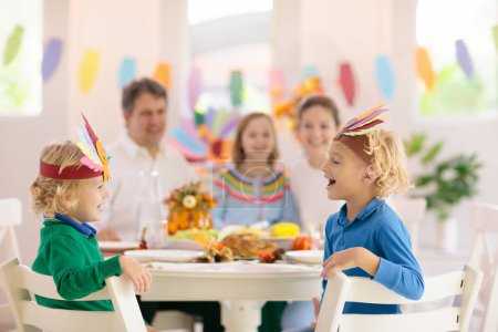 Photo for Family with kids eating Thanksgiving dinner. Roasted turkey and pumpkin pie on dining table with autumn decoration. Parents and children festive meal. Father and mother cutting meat. Paper crafts hat. - Royalty Free Image