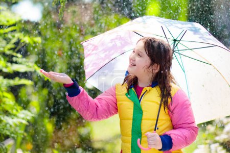Téléchargez les photos : Enfant jouant sous la pluie d'automne. Enfant avec parapluie. Petite fille courant dans un parc à l'automne. Amusement extérieur pour les enfants par tous les temps. Vêtements imperméables à l'eau, bottes et veste pour enfants. - en image libre de droit