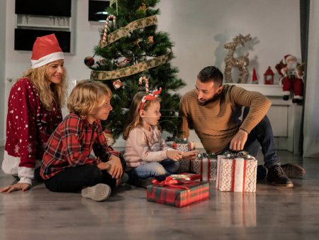 Téléchargez les photos : Heureuse famille caucasienne de quatre personnes réunie autour du sapin de Noël pour ouvrir des cadeaux - en image libre de droit