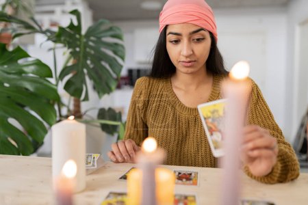 Junge Hindu-Frau beim Lesen von Tarotkarten mit Kerzen zu Hause. Indische Jahrtausendlesekarten für Frauen.