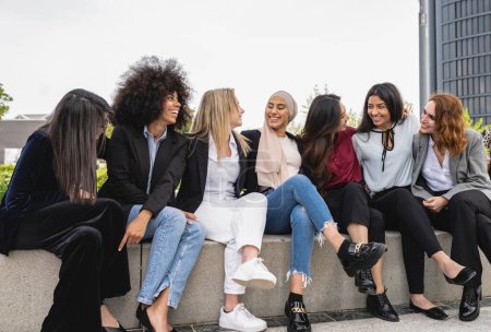 Foto de Grupo de mujeres multirraciales felices sentadas en trajes mirándose unas a otras - Imagen libre de derechos