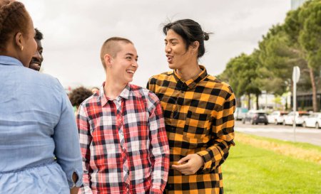 Zwei junge Menschen nicht binären Geschlechts genießen mit anderen Freunden in einem öffentlichen Park.