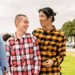 Two young people of non binary gender enjoy with other friends in a public park.