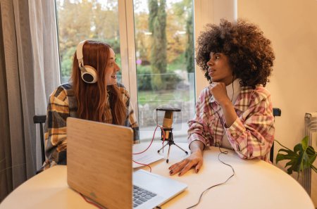 Two multiracial females with a microphone and headphones recording a podcast for social media. Influencers recording at home